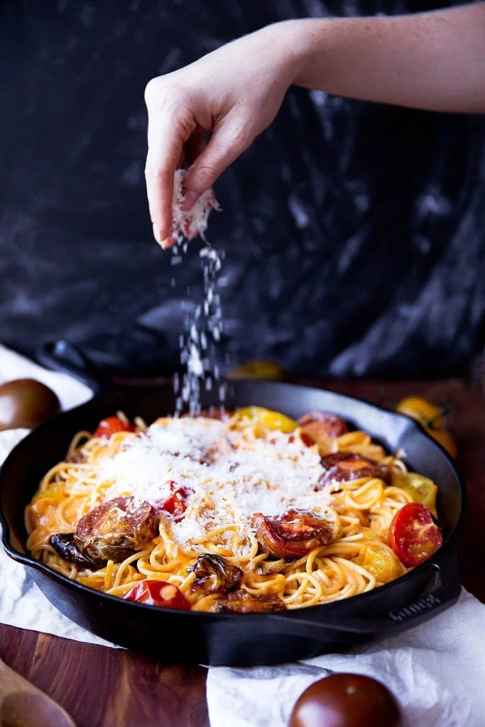 sprinkling parmesan onto spaghetti with tomato cream sauce