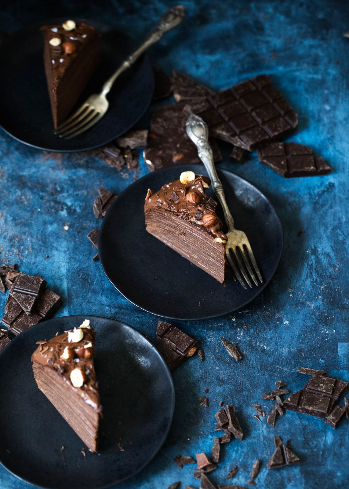 Hazelnut Chocolate Crepe Cake slices on plates with chocolate pieces