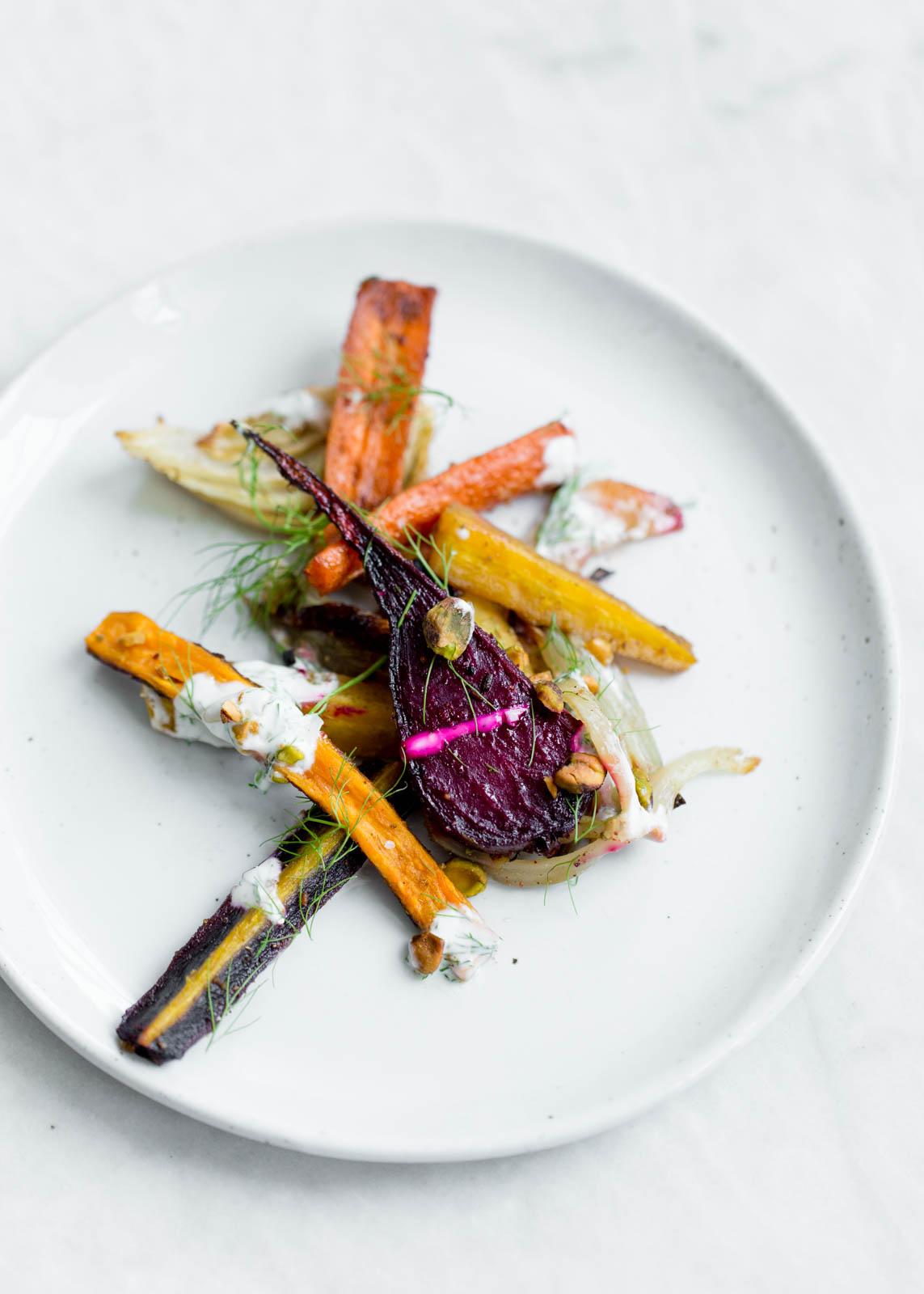 Perfectly caramelized Roasted Root Vegetables tossed in fennel and cumin and drizzled with pistachio yogurt and fennel fronds.