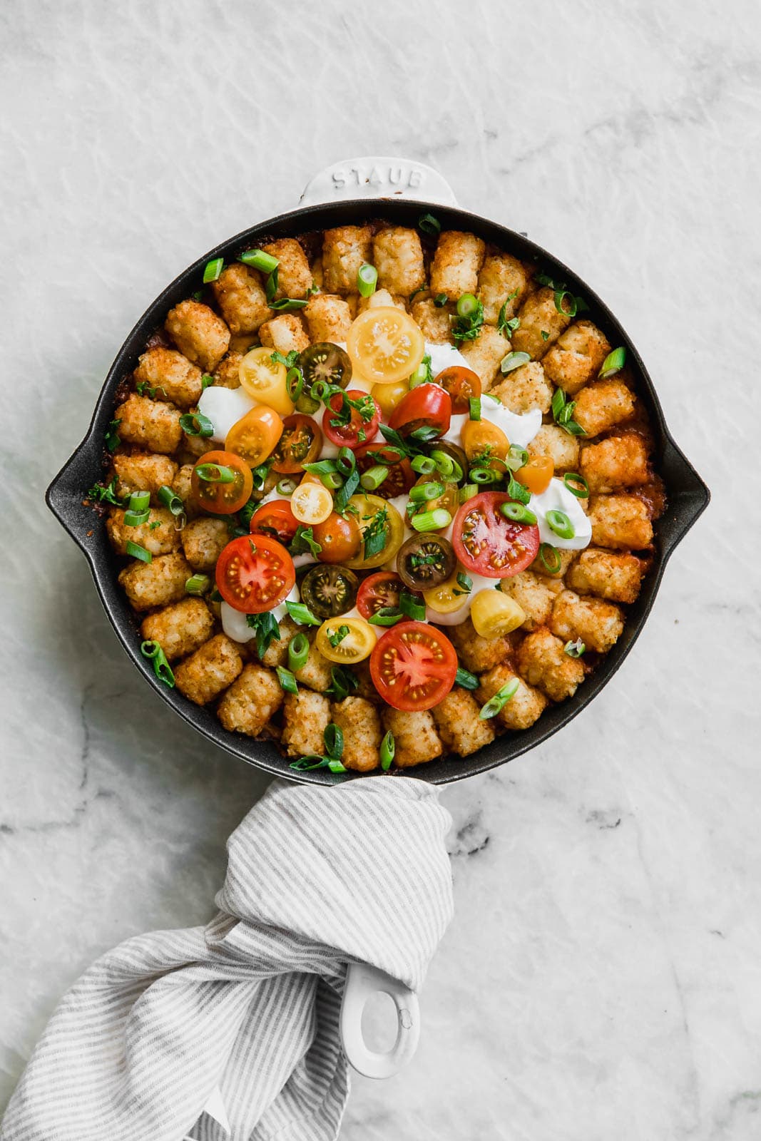 tater tot casserole topped with cherry tomatoes and sour cream