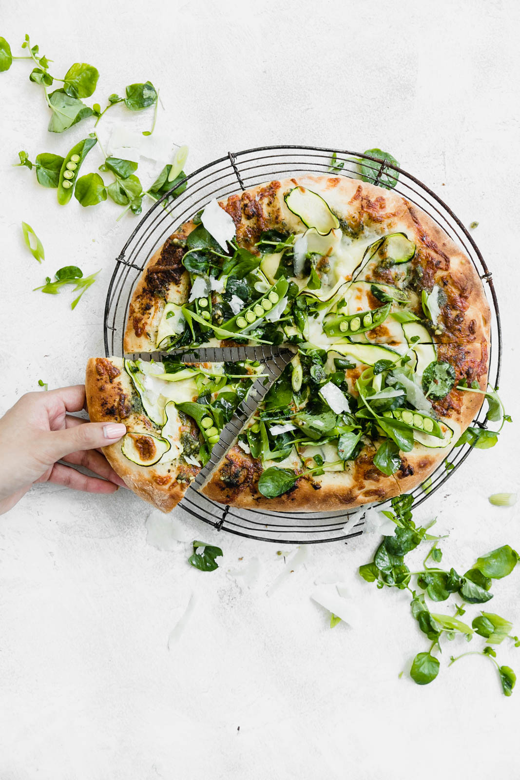 A Spring Green Goddess Pizza made with pesto, zucchini, spring peas, watercress, mozzarella, and a green goddess dressing.
