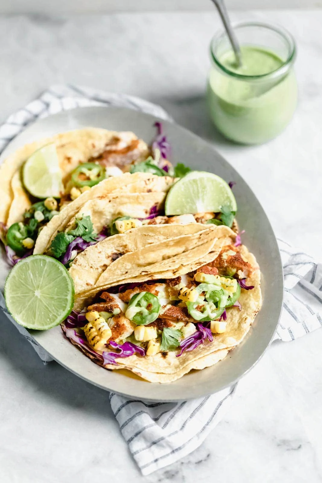 My go-to recipe for Taco Tuesday fish tacos: flakey blackened fish, cabbage, charred corn, jalapeños, and a “creamy” dairy-free avocado cilantro crema!