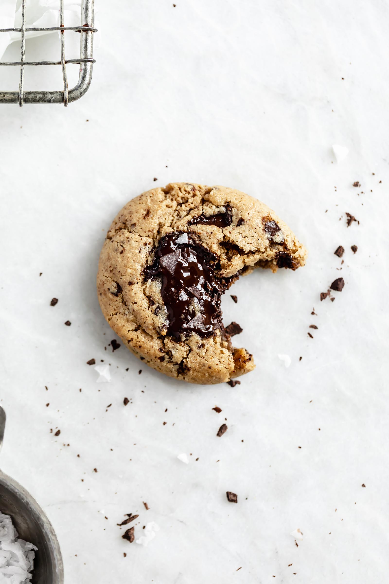 healthy gluten free chocolate chip cookie with a bite taken out on parchment paper with crumbs