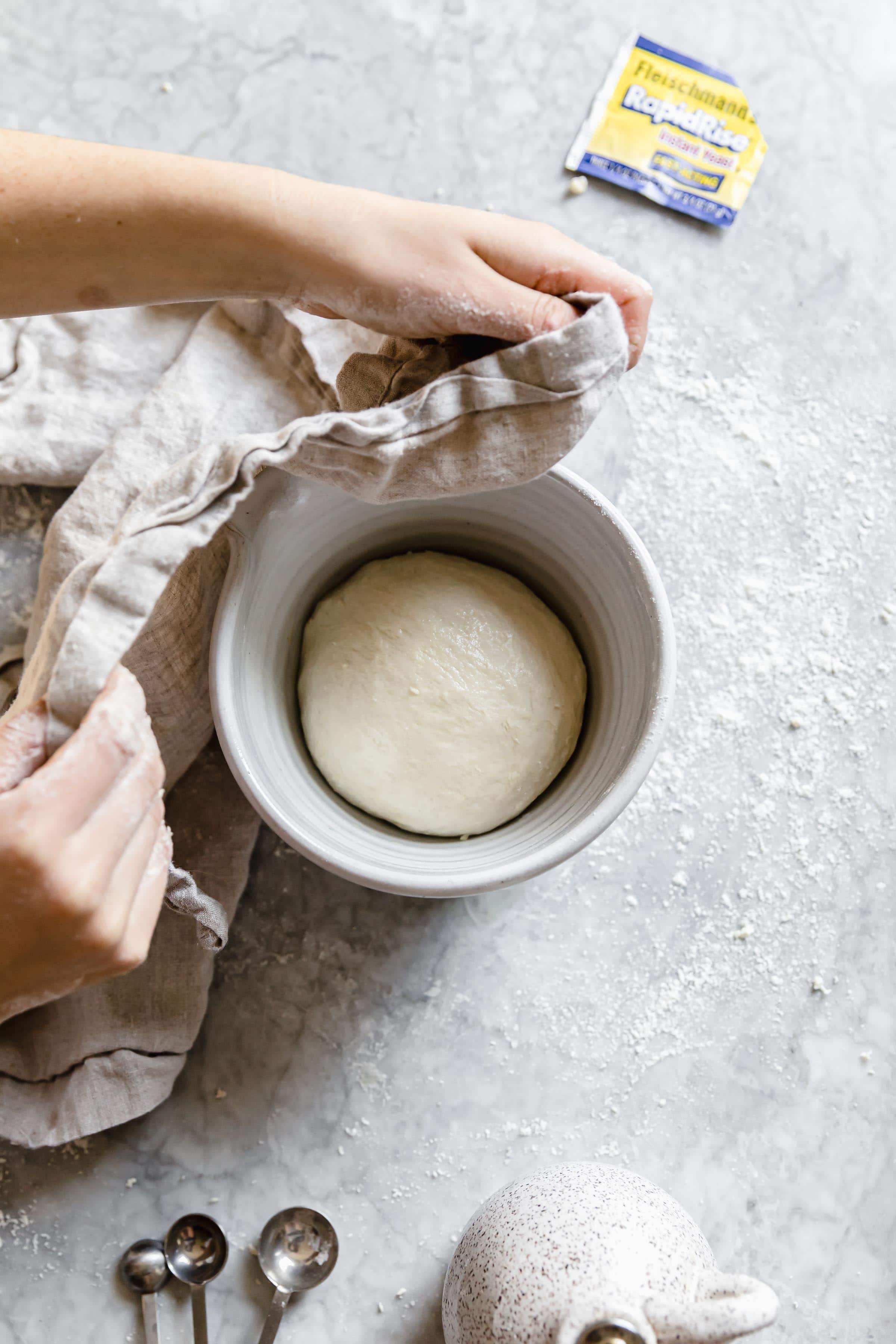 pizza dough resting in a warm place covered with dish cloth