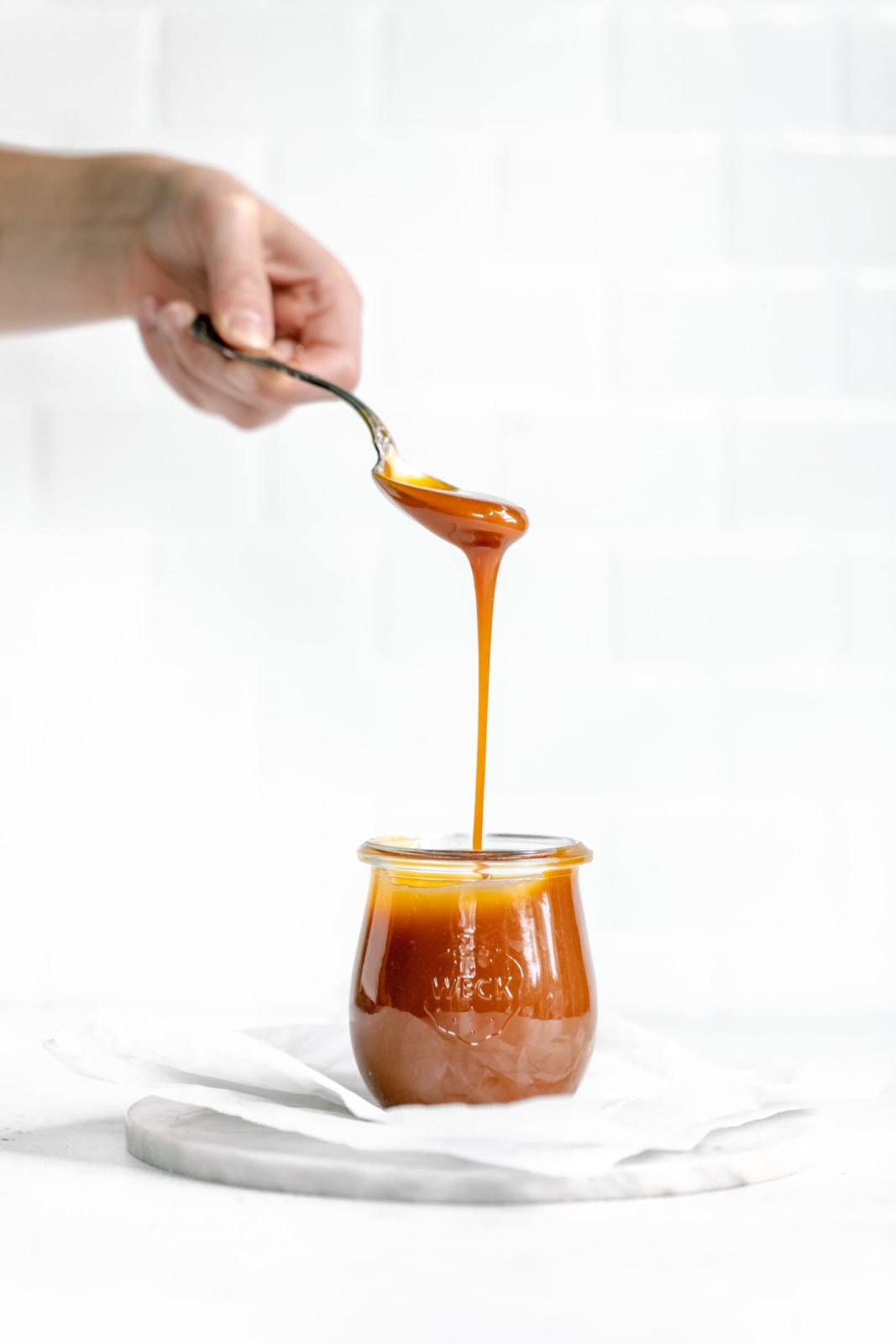 homemade caramel falling off of spoon into jar