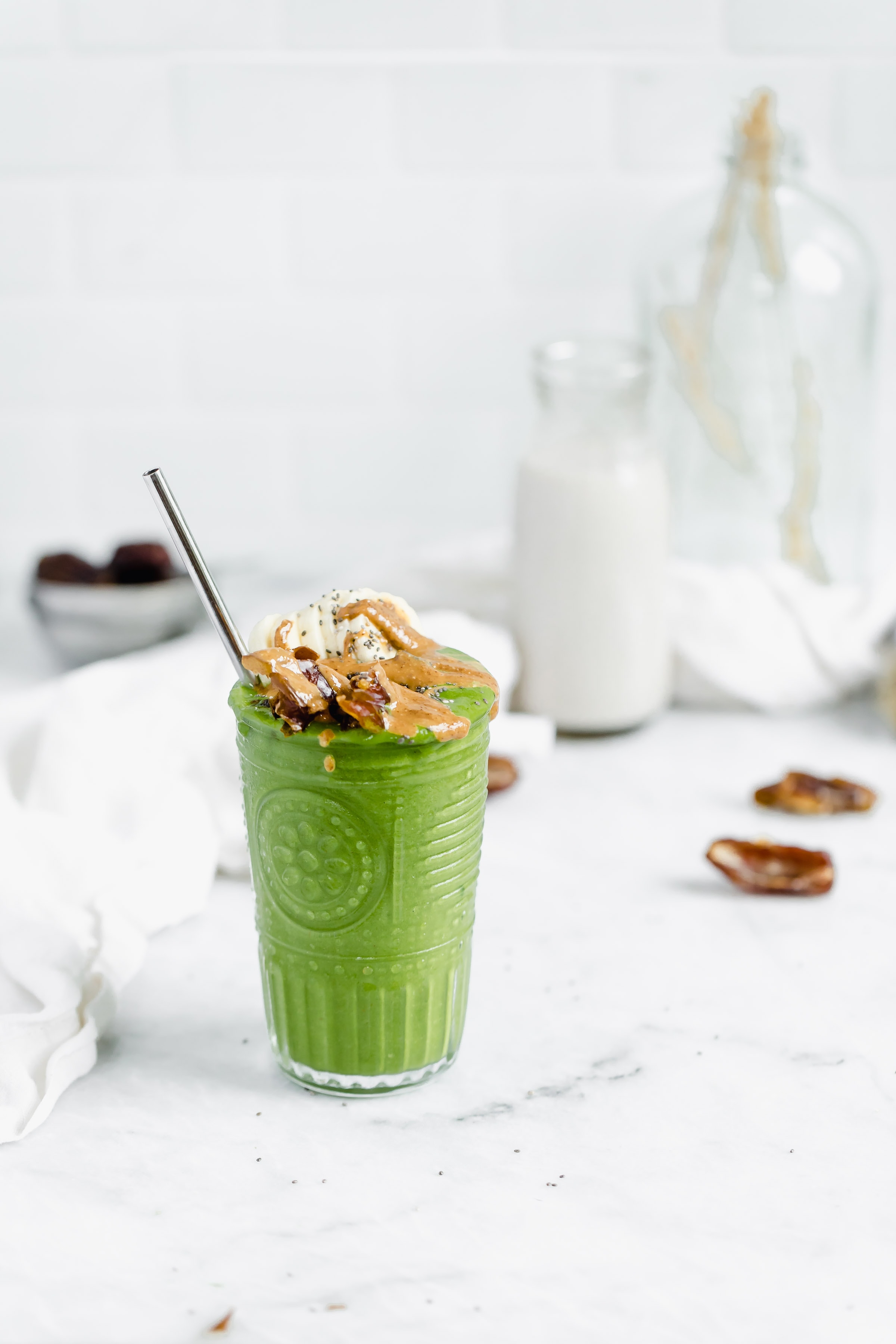 green smoothie topped with bananas, dates, almond butter, and chia seeds
