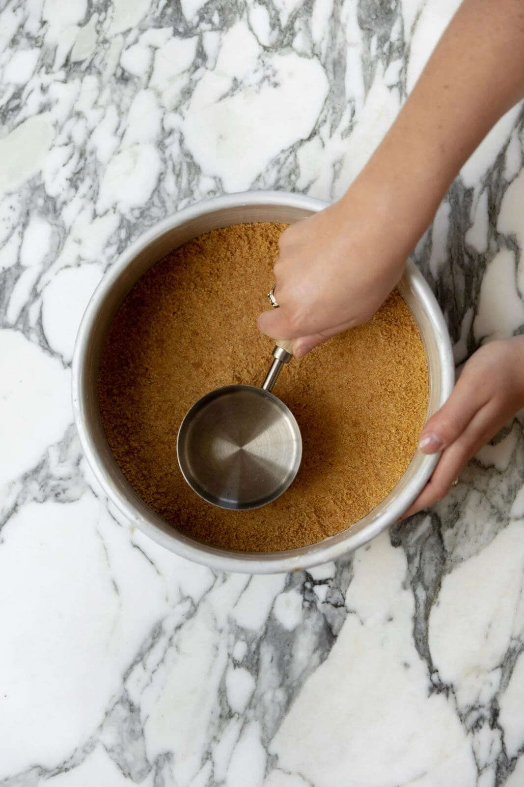 measuring cup packing graham cracker crust into an even layer
