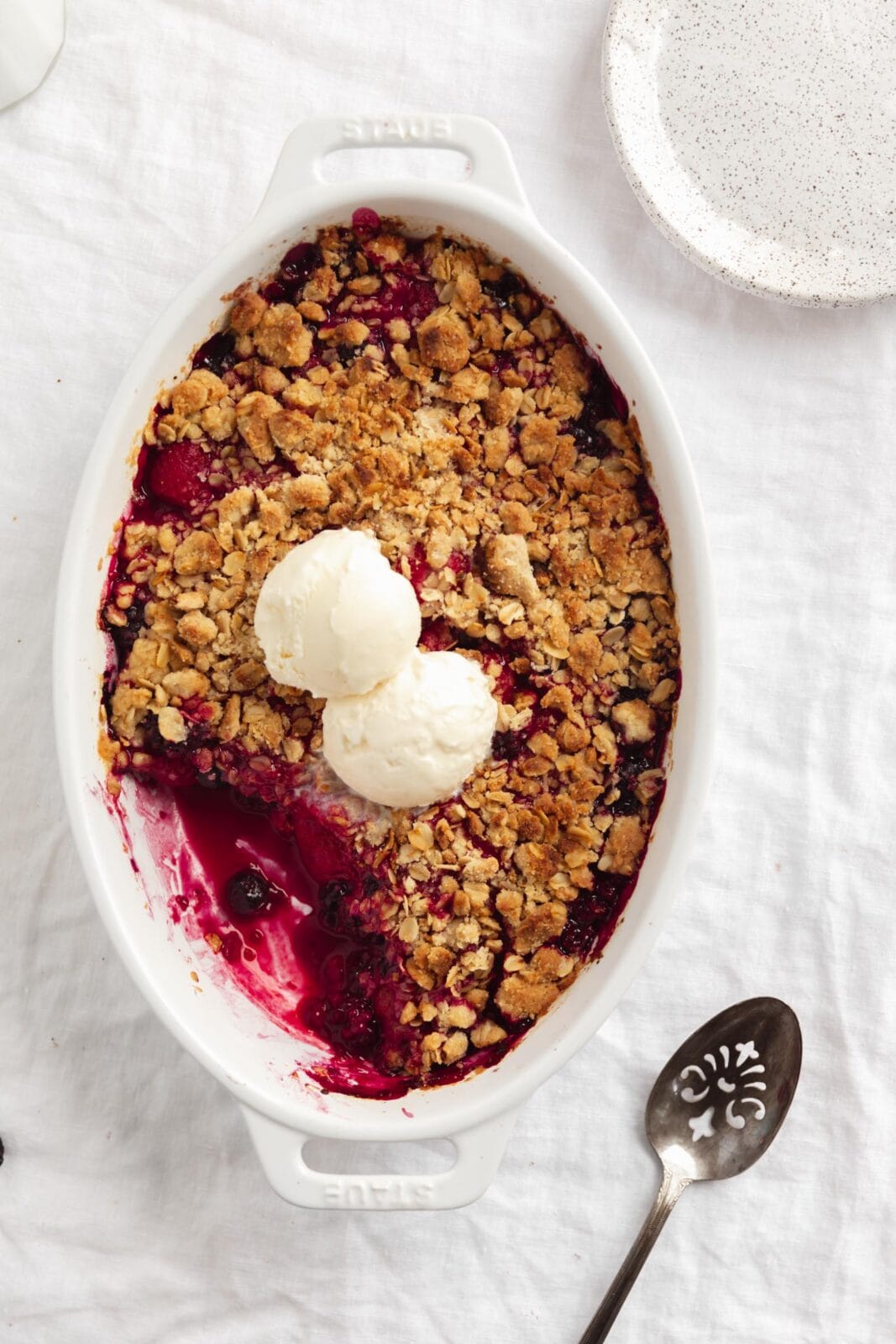 mixed berry crisp in a white dish with ice cream