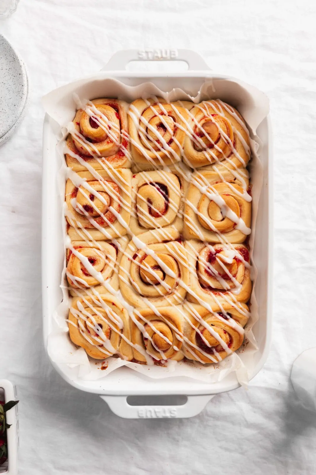 strawberry sweet rolls drizzled with frosting in a white pan