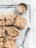cinnamon roll blondies with cinnamon sugar and spoonful of icing on a cooling rack